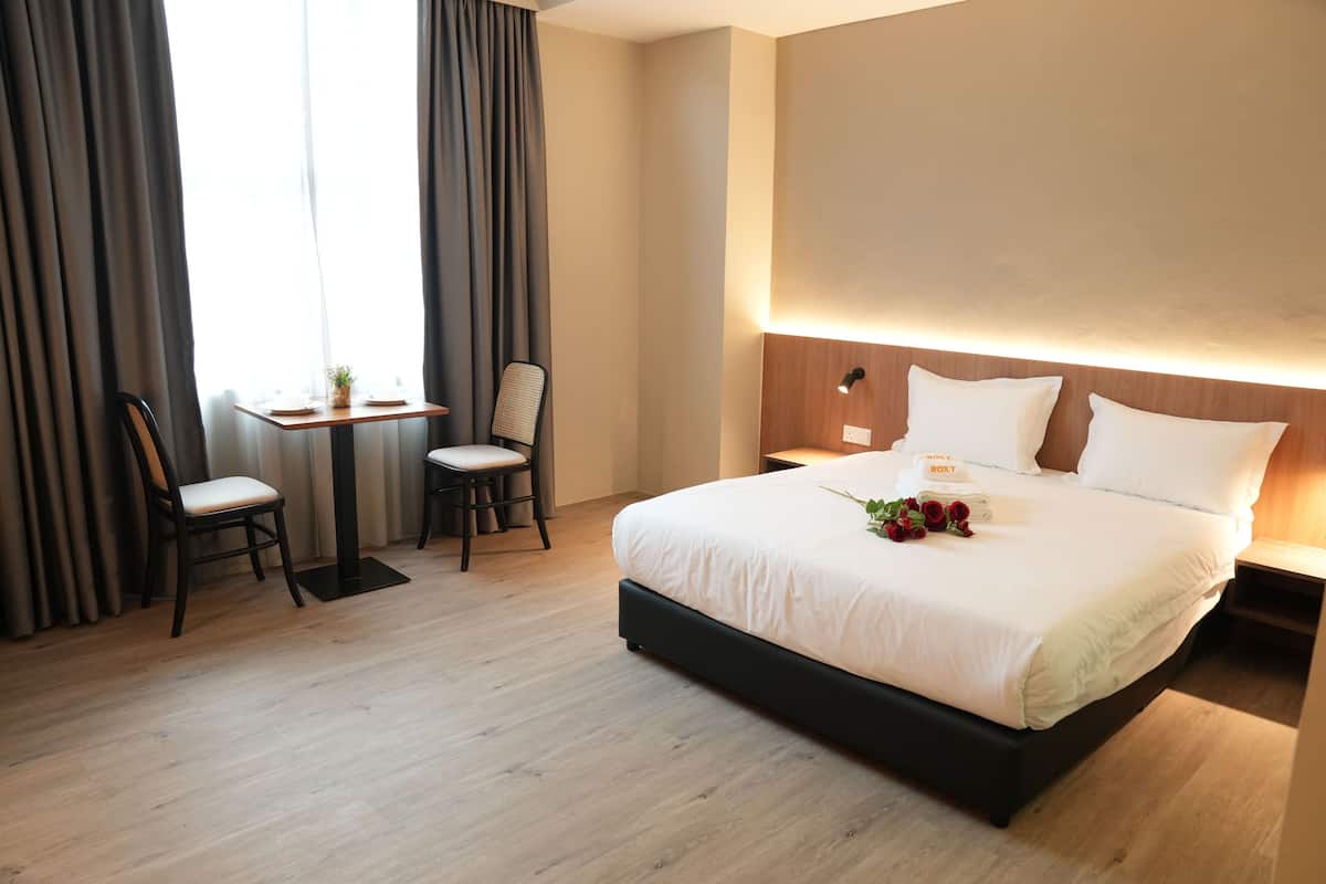 A hotel room with a large bed, a desk with two chairs, and a window with curtains.