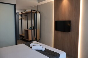 Habitación de hotel moderna con cama, televisor montado en la pared y armario de madera.