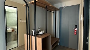 Habitación de hotel moderna con tocador de madera, un espejo grande y una puerta con señal de salida de emergencia roja.