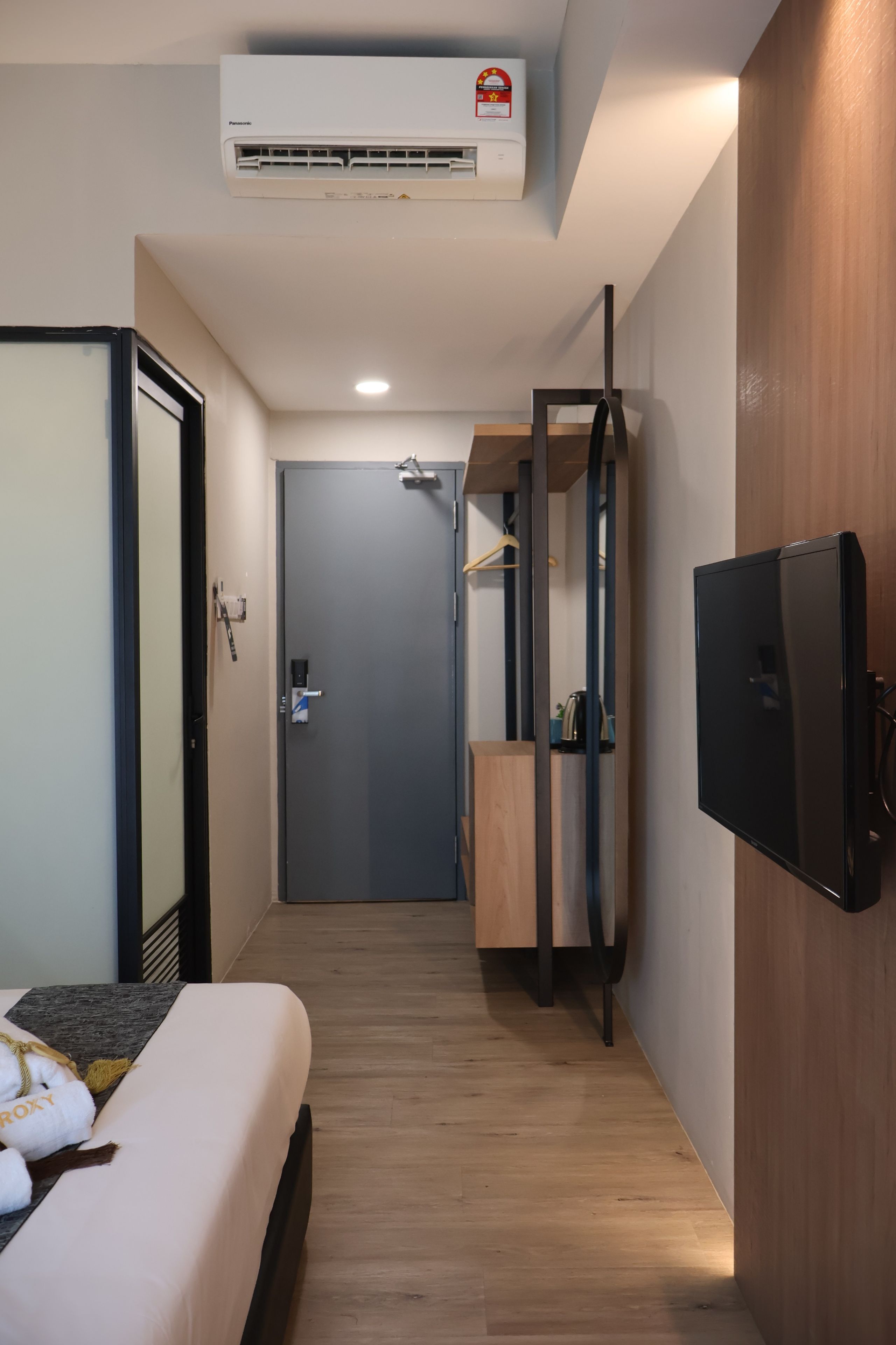Habitación de hotel con cama, televisor, aire acondicionado, armario de madera y puerta que da a un baño.