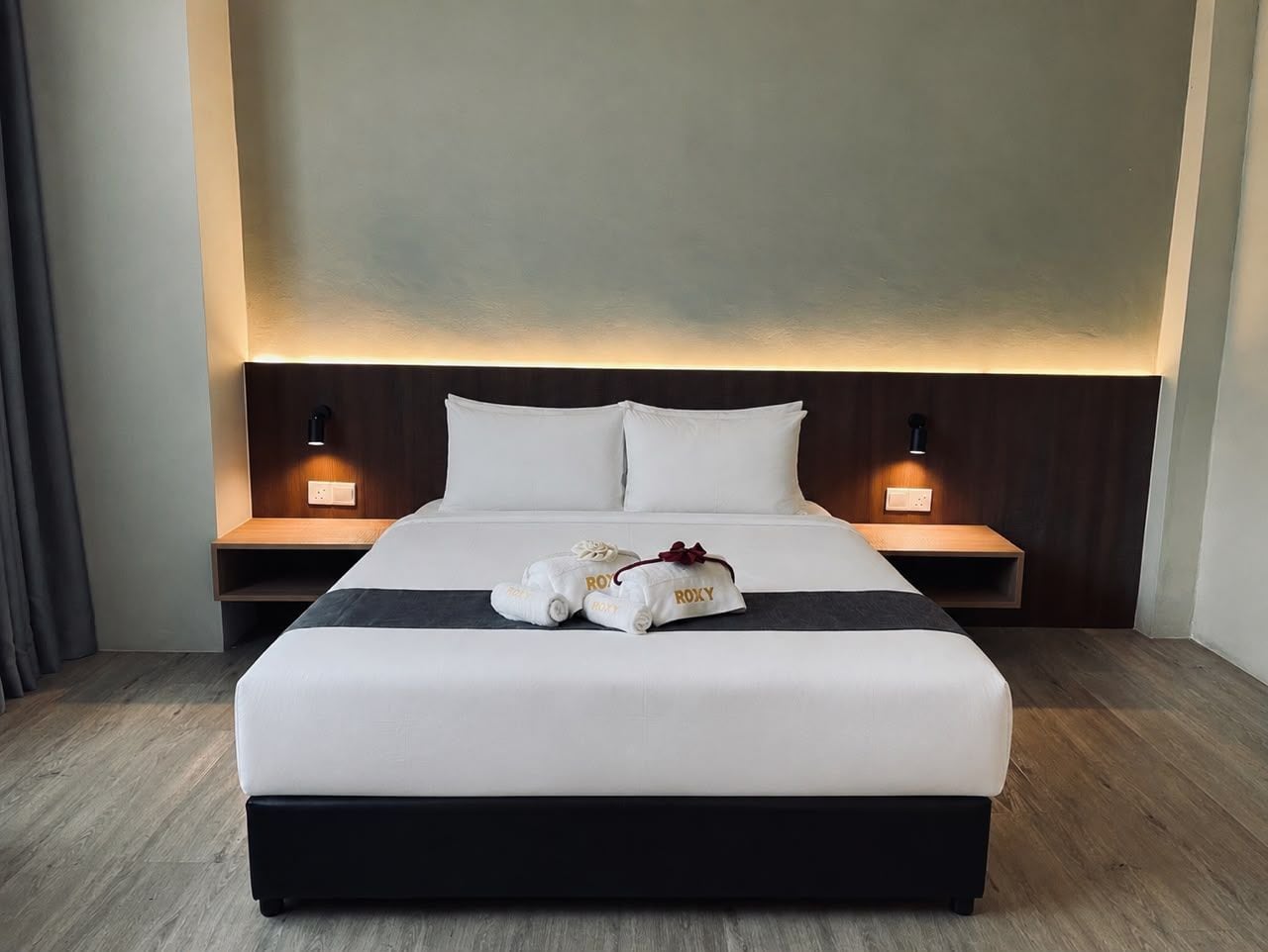 A neatly made bed with white linens and two pillows, a bedside table with a lamp, and a wall-mounted light fixture.