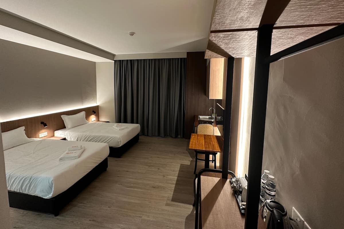 A hotel room with two beds, a small desk, a mirror, and a minibar.
