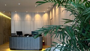Un mostrador de recepción moderno con suelo de madera, una planta en maceta grande y un equipo de aire acondicionado instalado en la pared.