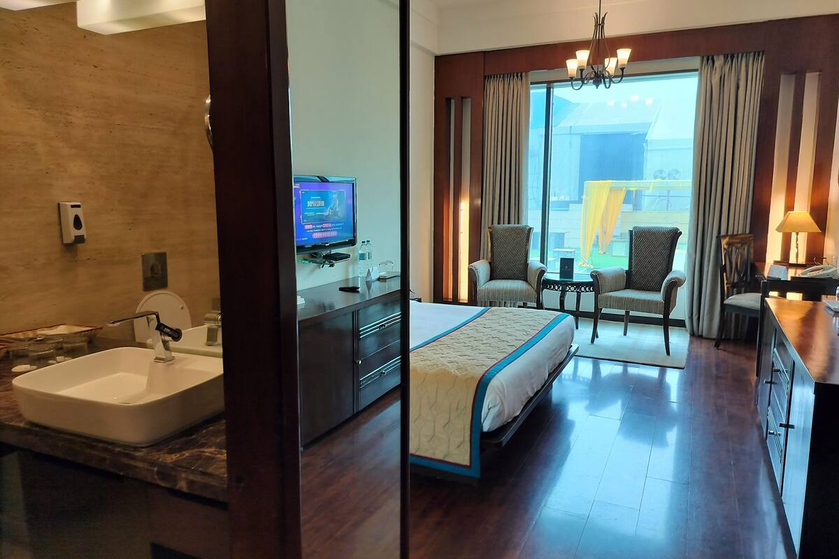 A hotel room with a large bed, a desk with a chair, a TV, a bathroom with a bathtub, and a view of the outside.