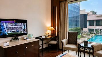 A hotel room with a television, desk, chairs, a bed, and a view of a swimming pool.