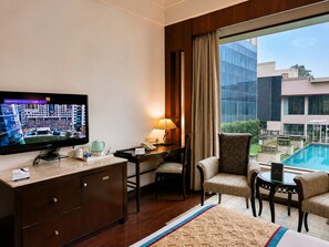 Habitación de hotel con televisión, escritorio, sillas, cama y vista a una piscina.