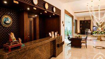 A hotel reception area with a marble counter, clocks, and a chandelier.