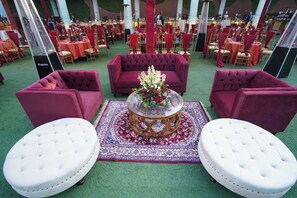 Un espacio para eventos formales con mobiliario rojo y blanco, incluyendo sofás y otomanas, dispuesto alrededor de una mesa central con un arreglo floral.