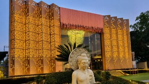 A building with a large Buddha statue in front, surrounded by a well-maintained garden with a water feature.