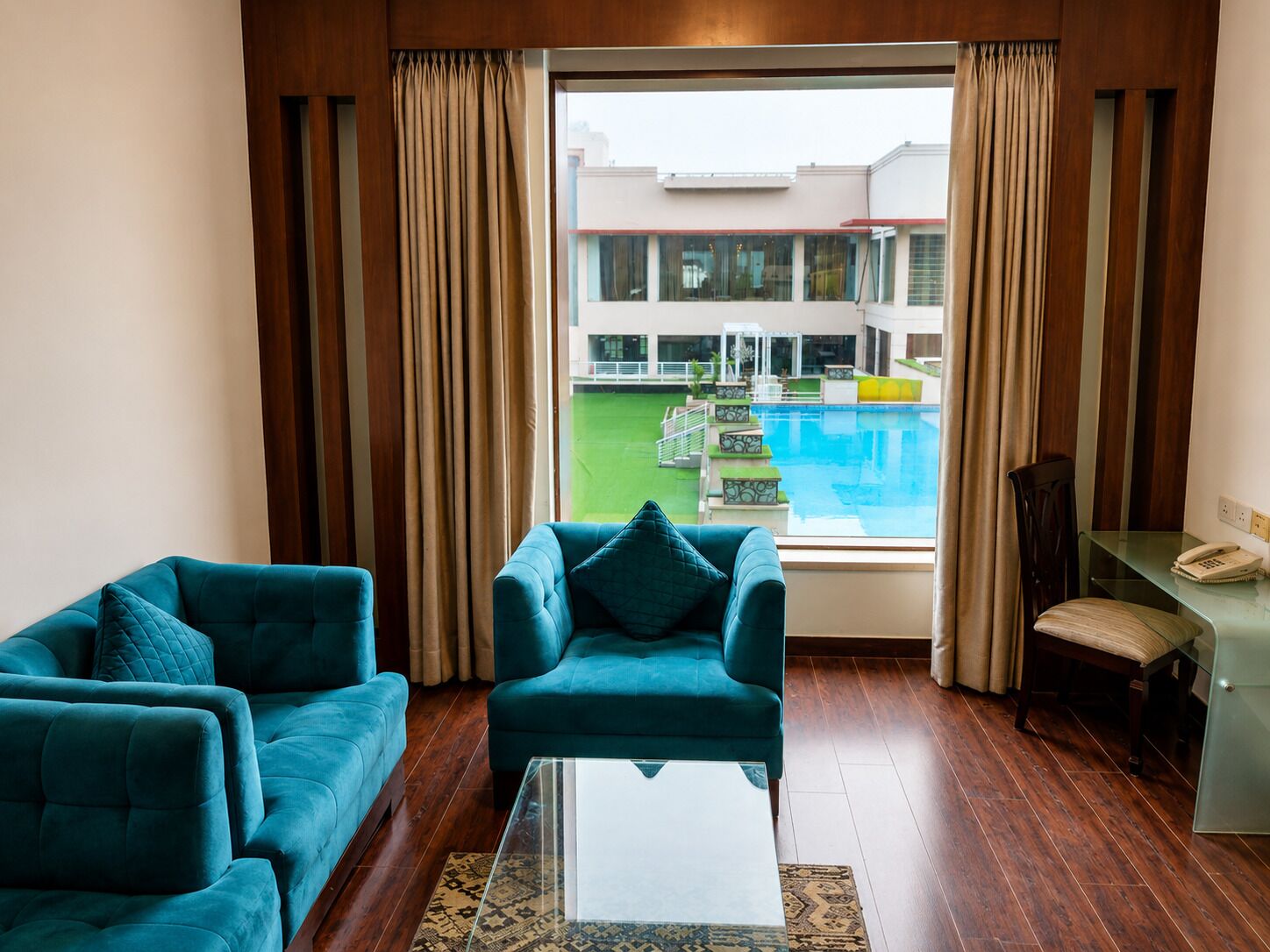 A hotel room with a view of a swimming pool and a building complex.