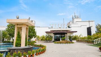 A hotel entrance with a pool, potted plants, and a clear sky.