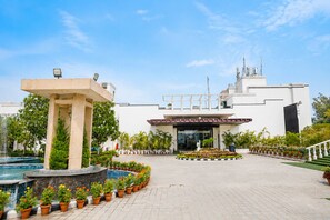 Entrada de hotel con piscina, plantas en macetas y cielo despejado.