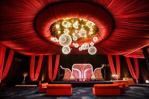 A theater with red curtains, a stage with a red and white backdrop, and a chandelier.