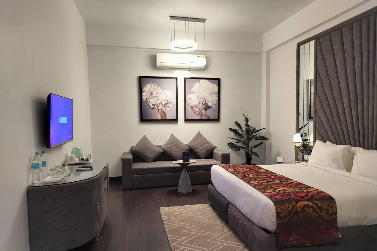 A modern hotel room with a bed, a sofa, a TV, and artwork on the wall.