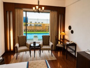 Habitación de hotel con cama, dos sillones, una mesita, un escritorio con lámpara y vista a una piscina.