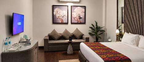 Quarto de hotel com cama, sofá, escrivaninha, televisão e obras de arte na parede.