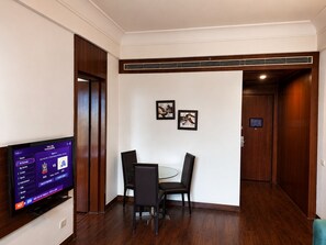 Habitación de hotel con televisor de pantalla plana mostrando contenido deportivo, una mesa de comedor con sillas y una puerta de madera.