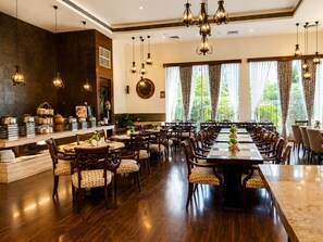 A spacious dining area with multiple tables and chairs, a buffet setup on the left, and large windows with curtains. - Bel-La Monde Hotel NH8 at 6km from IGI Airport Delhi (New Delhi)