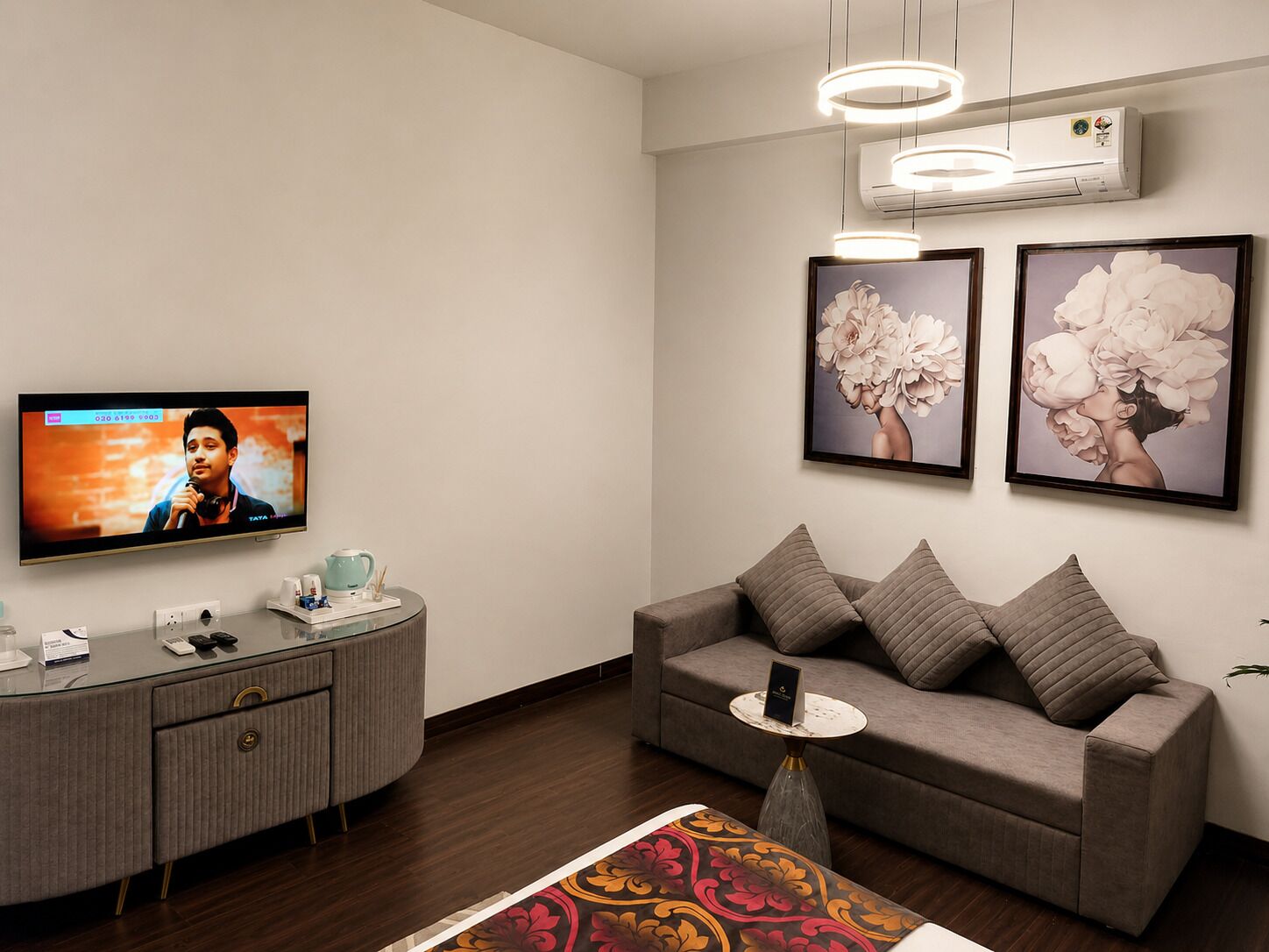 A modern living room with a flat-screen TV, a grey sofa, a coffee table, and framed floral artwork on the wall.