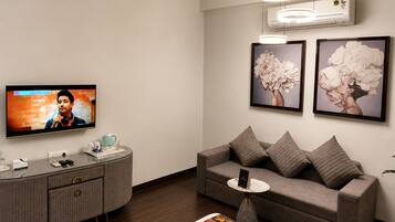 A modern living room with a flat-screen TV, a grey sofa, a coffee table, and framed floral artwork on the wall.