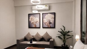 A hotel room with a bed, a sofa, a coffee table, a potted plant, and two framed artworks on the wall. - Bel-La Monde Hotel NH8 at 6km from IGI Airport Delhi (New Delhi)