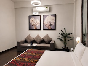 Una habitación de hotel con una cama, un sofá, una mesita de centro, una planta en maceta y dos cuadros en la pared.