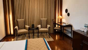 Habitación de hotel con cama, dos sillones, un escritorio con lámpara, teléfono y un armario con botellas de agua.