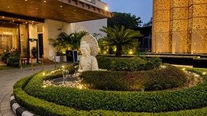 A well-maintained garden with a Buddha statue, surrounded by neatly trimmed hedges and a fountain.