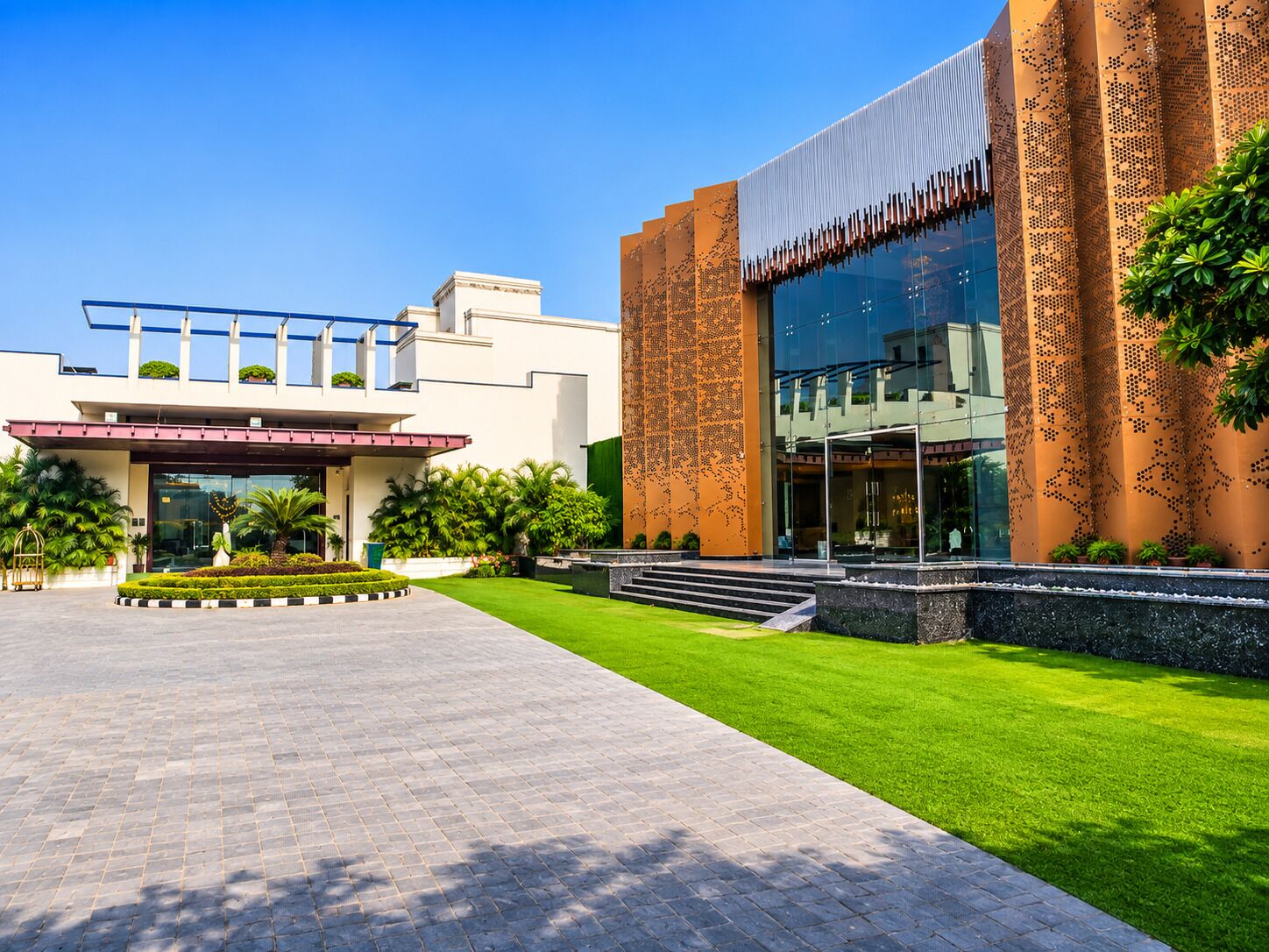 A modern building with a large glass facade, a well-maintained lawn, and a clear sky.