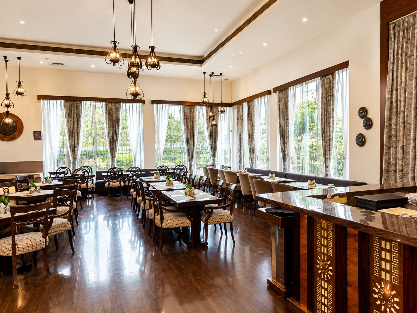 Un comedor amplio con varias mesas y sillas, ventanas grandes con cortinas e iluminación colgante.
