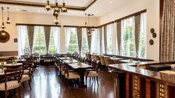 Un comedor amplio con varias mesas y sillas, ventanas grandes con cortinas e iluminación colgante.