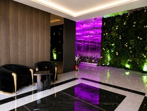 A modern lobby with a black and white tiled floor, a black sofa with gold accents, and a wall with a vertical garden and purple lighting.