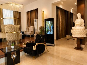 A modern lobby with a black sofa, a golden chair, a large screen, and a statue.