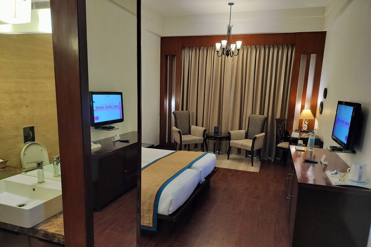 Habitación de hotel con cama, escritorio, silla, televisor y baño.