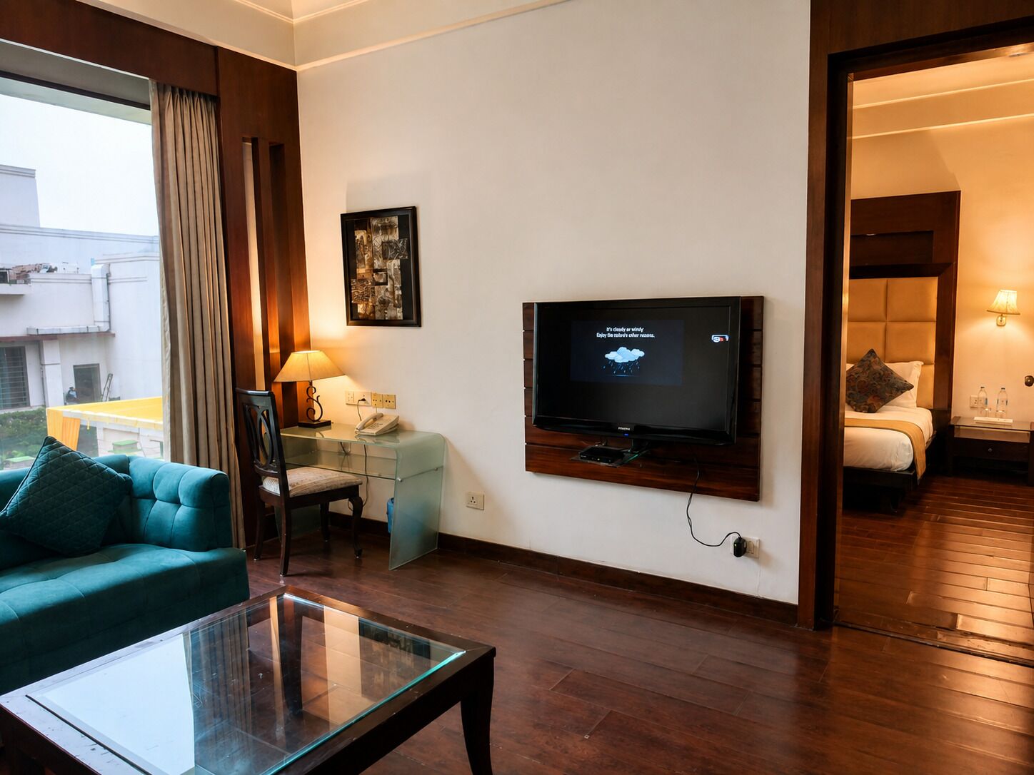 A hotel room with a television, a desk with a lamp, a sofa, and a bed.