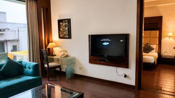 A hotel room with a television, a desk with a lamp, a sofa, and a bed.