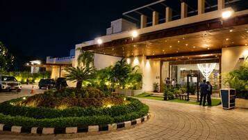 A hotel entrance with a covered walkway, palm trees, and a parking area.