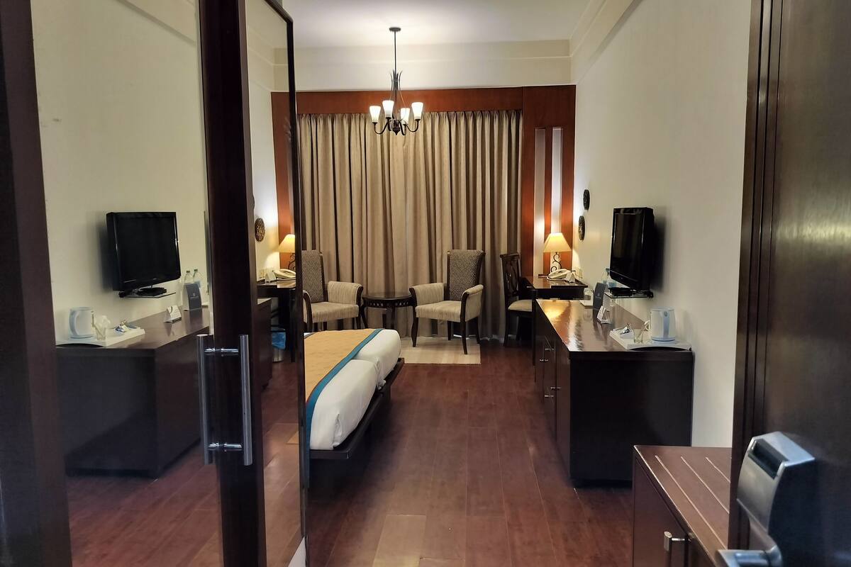 A hotel room with a bed, a desk, a chair, a television, and a desk lamp.