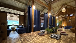 Ein geräumiges Zimmer mit Holzboden, blauen Vorhängen und einer Projektionsleinwand.