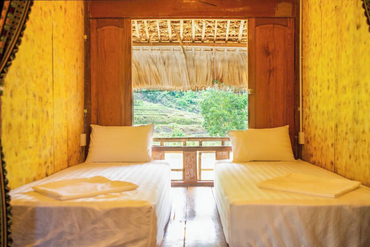 A room with two beds, a window with a view of a green landscape, and wooden walls.