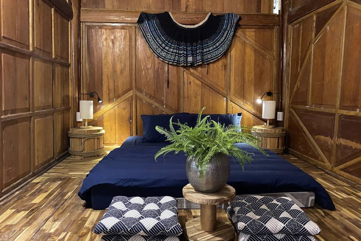 A room with a bed, wooden walls, a hanging decorative piece, and two nightstands with lamps.