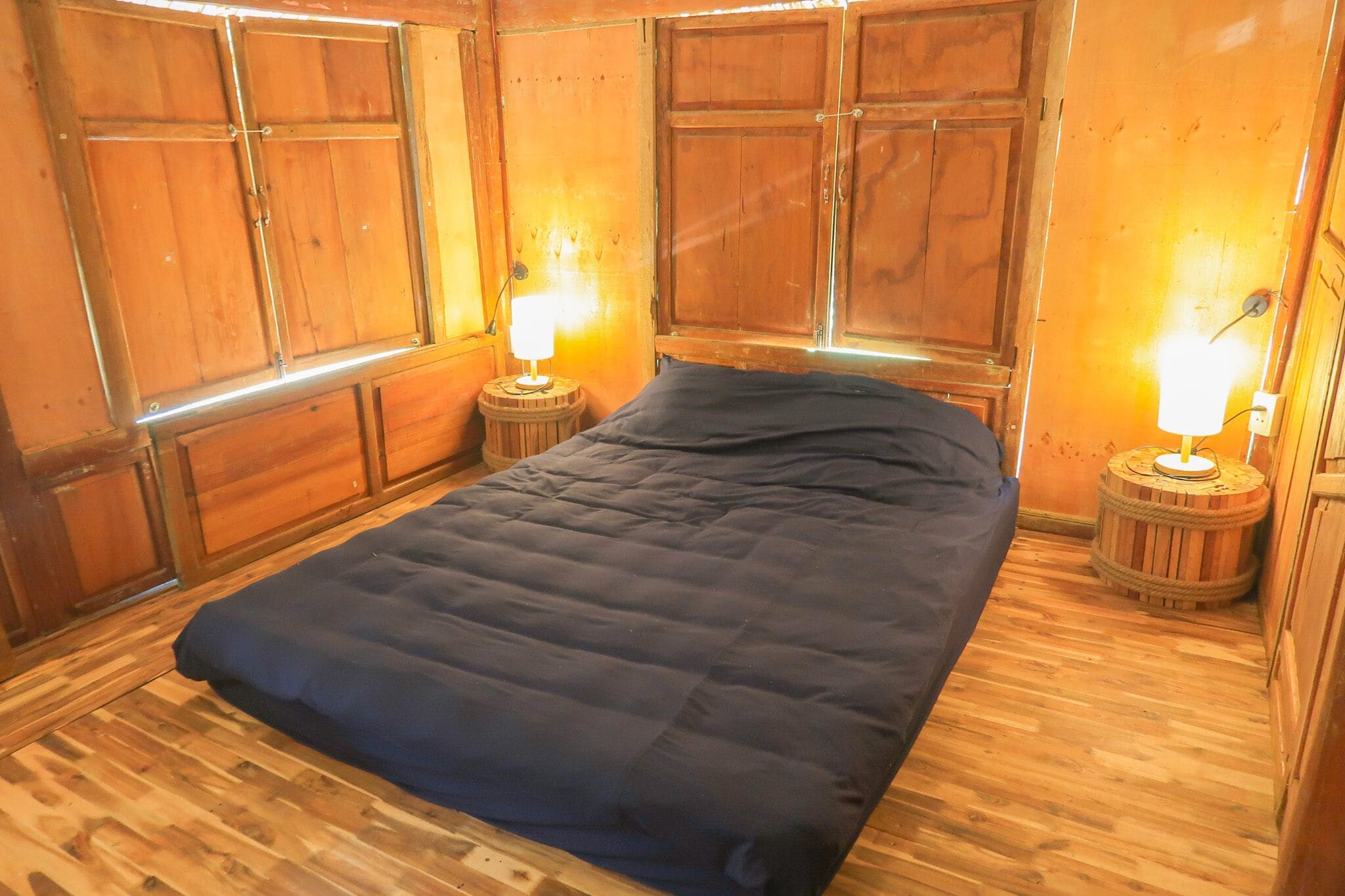 A wooden-paneled room with a bed, two nightstands with lamps, and a window.