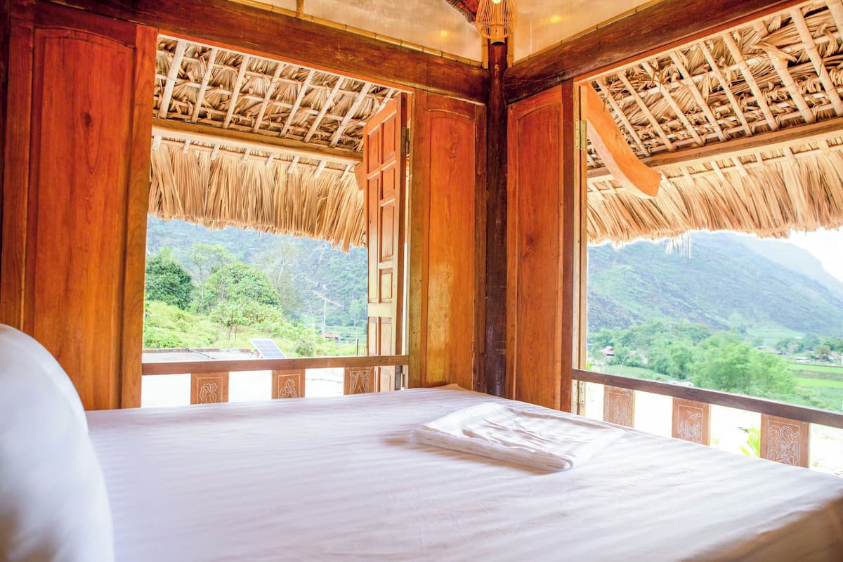 A room with a bed, wooden walls, and a view of a green landscape through a window.