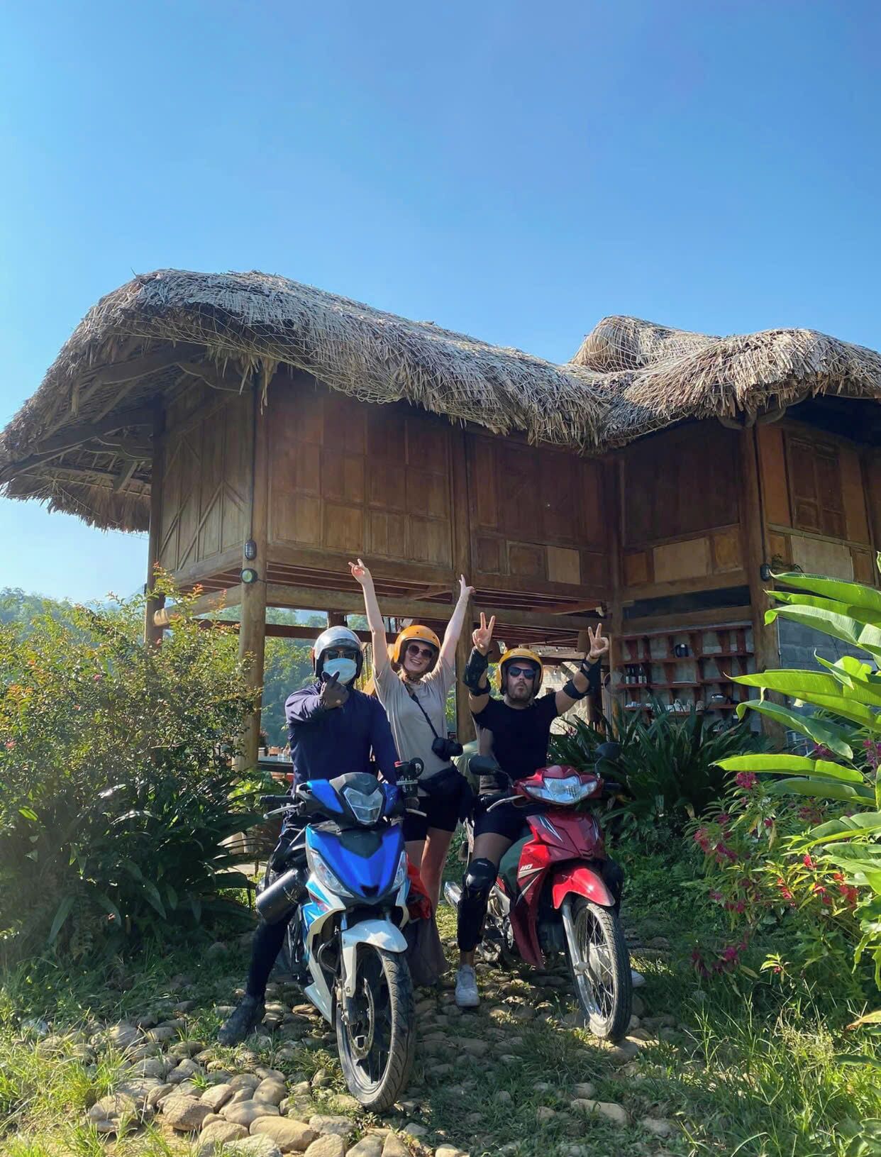 A rustic wooden structure with a thatched roof, surrounded by greenery.