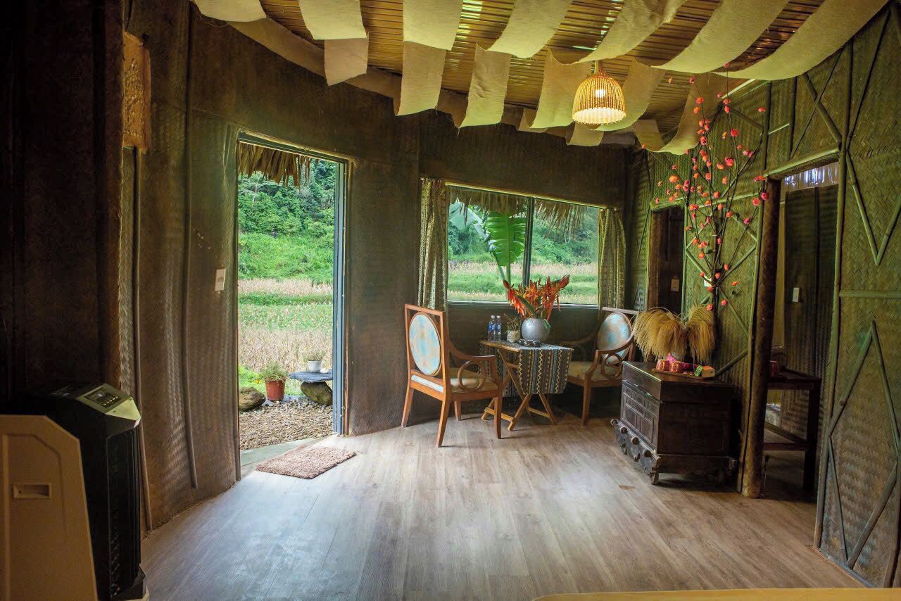 A room with a wooden floor, a table with chairs, a vase with flowers, and a window with a view of greenery.