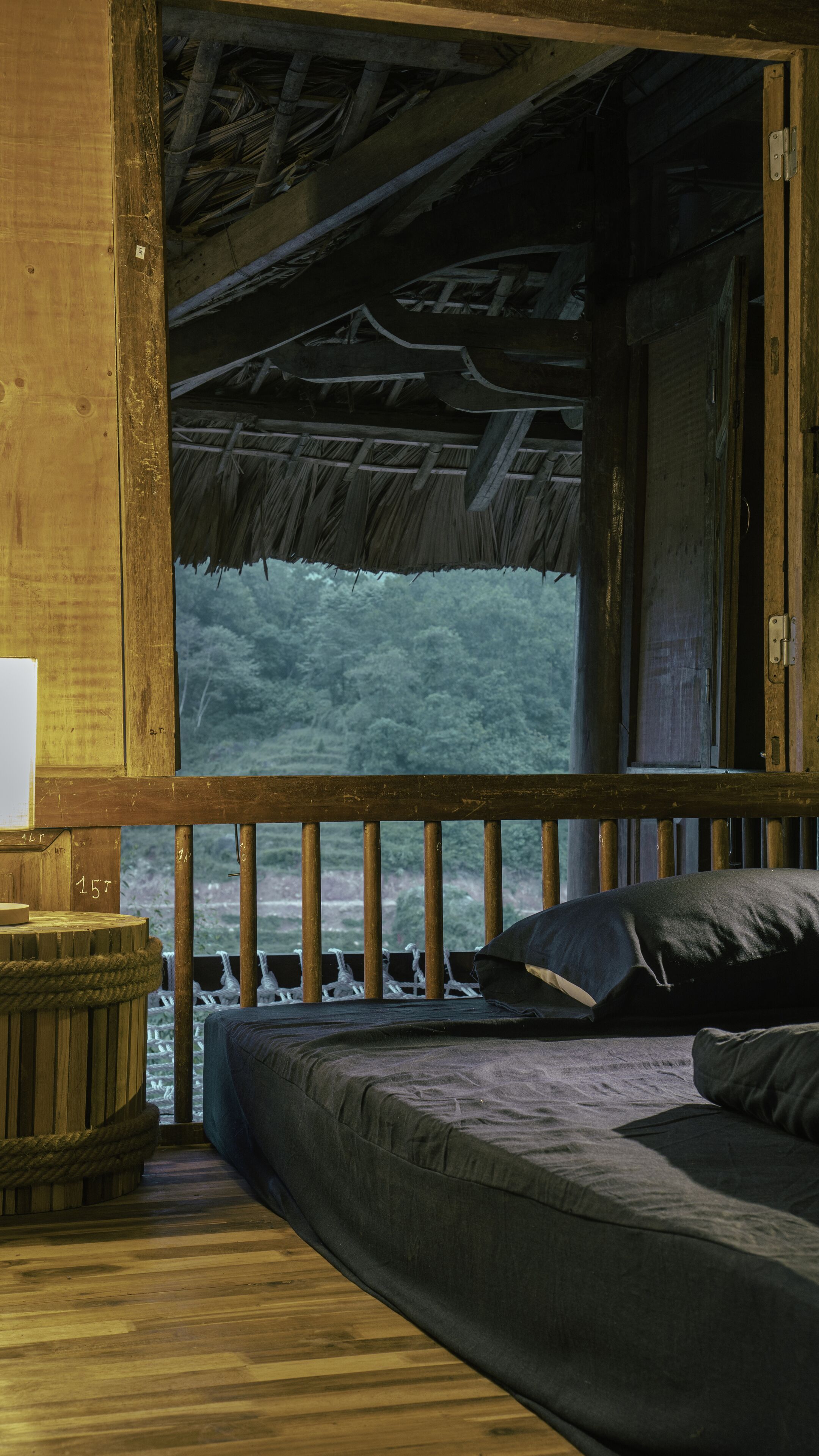 A wooden cabin with a bed, a small table, and a view of a forest through a large window.