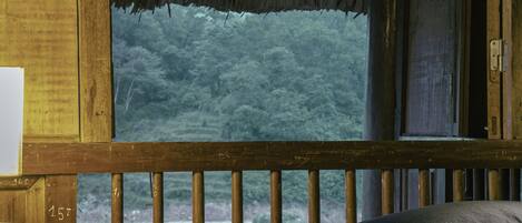A wooden cabin with a bed, a small table, and a view of a forest through a large window.