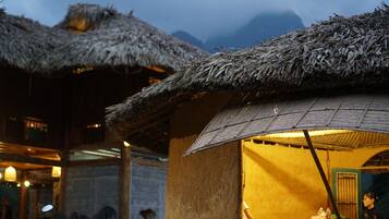 A rustic hut with a thatched roof, a small window, and a person inside.
