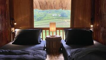 Een kamer met twee bedden, een houten vloer, een rieten plafond en uitzicht op een groen landschap.