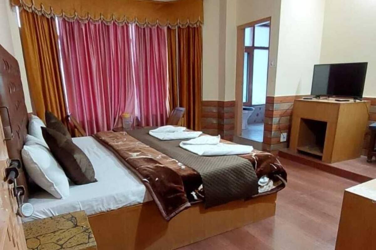 Habitación de hotel con cama, cortinas, televisor y suelo de madera.